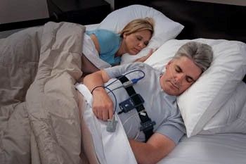 Image of patient having a sleep study while sleeping in his own bed. A variety of sensors transmit information to the device shown here.