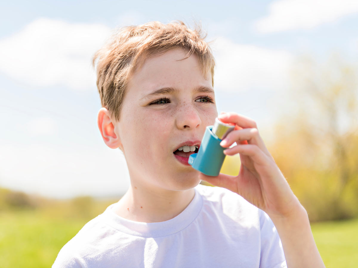 Child using an inhaler outdoors to manage allergic asthma symptoms triggered by environmental allergens.