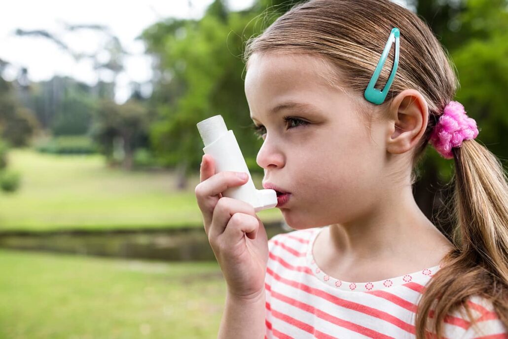 Little girl using her asthma inhaler outdoors