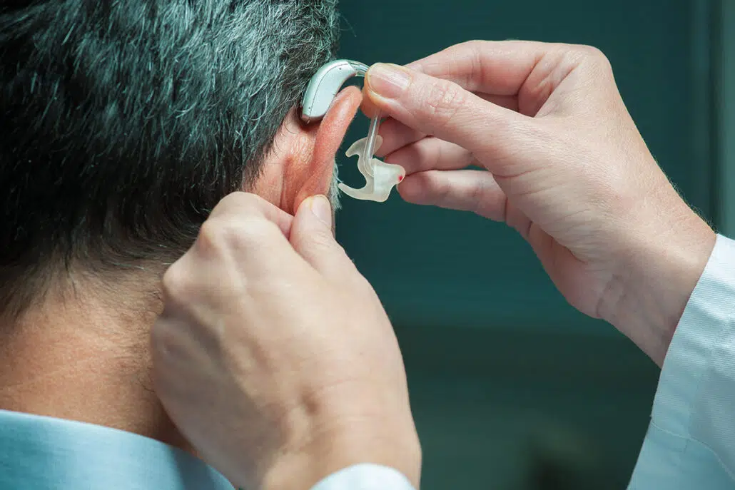 Close up to a doctor's hands placing a Hearing Aid on the right ear a patient with Hearing Loss