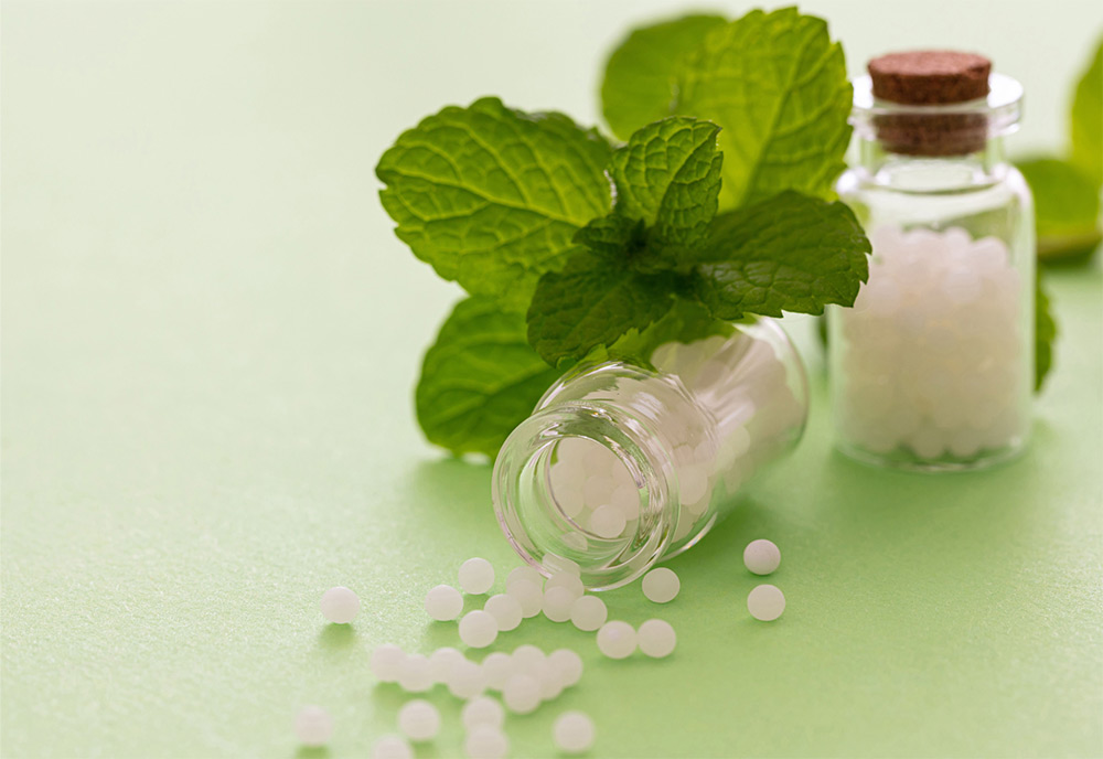 Homeopathic medicine bottles with white pellets and fresh mint leaves on a green surface.