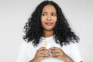 Concerned woman holding blister packs of medication, unsure about penicillin allergy symptoms.