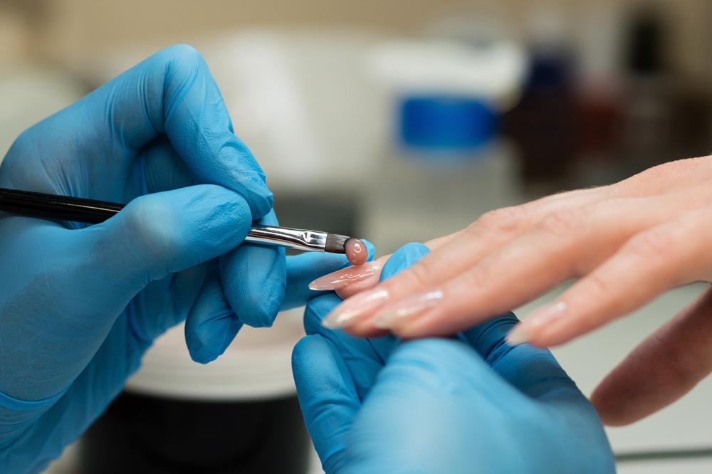 nail technician wearing nitrile gloves applying gel product on client's nails for allergy-safe manicure