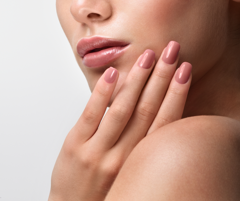woman with smooth skin and glossy pink hypoallergenic gel nails touching her face gently to show irritation-free style