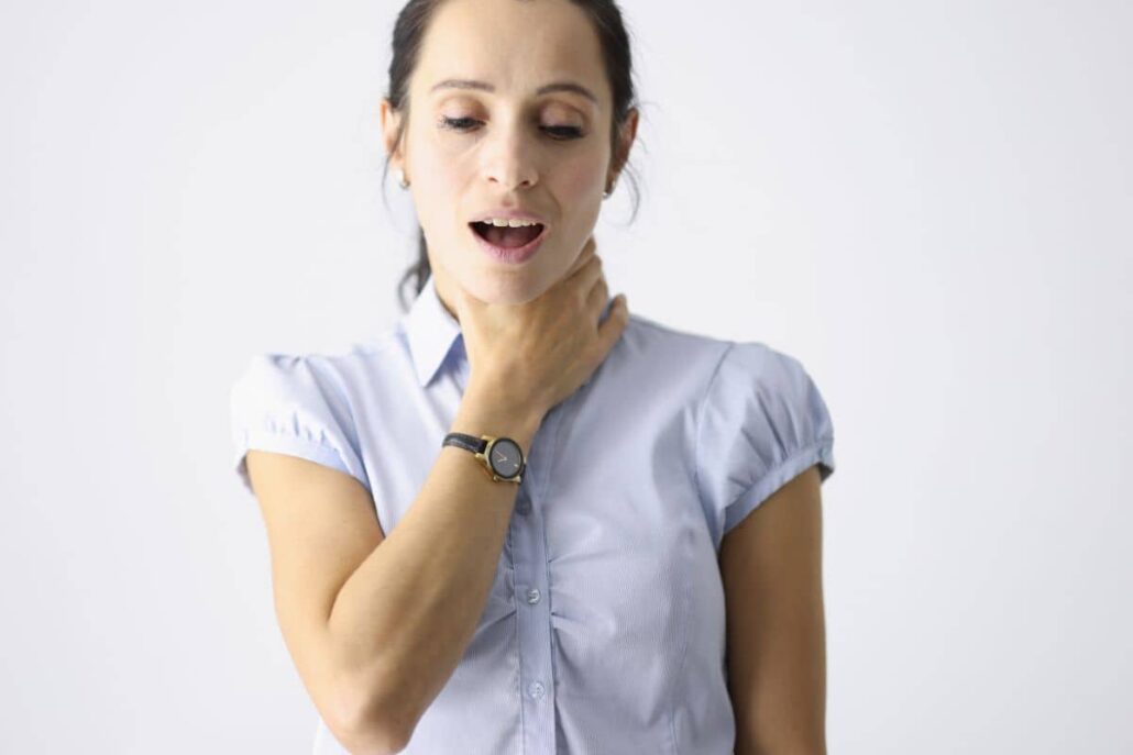 Woman holding her throat mid-speech, showing signs of discomfort often linked to vocal strain or hoarseness.