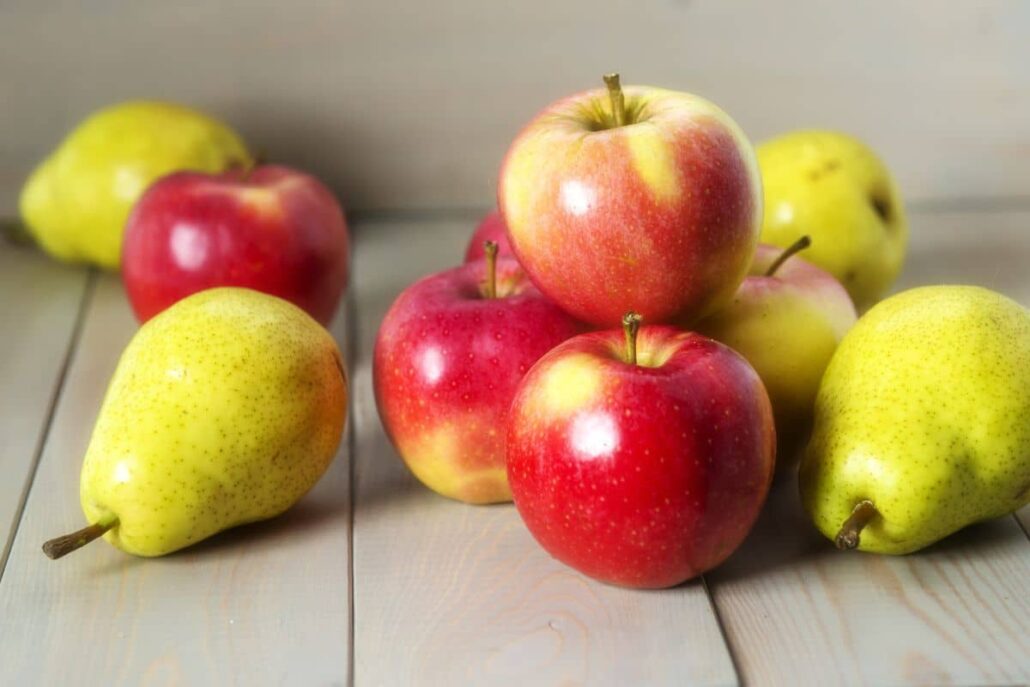Fresh apples and pears on a wooden table, common birch pollen cross-reactive foods causing oral allergy symptoms.
