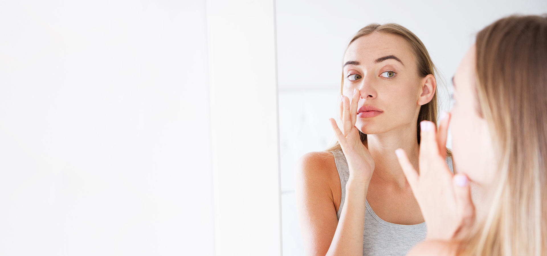Woman examining nose in mirror, illustrating awareness of nosebleeds, their causes, treatment, and prevention methods.