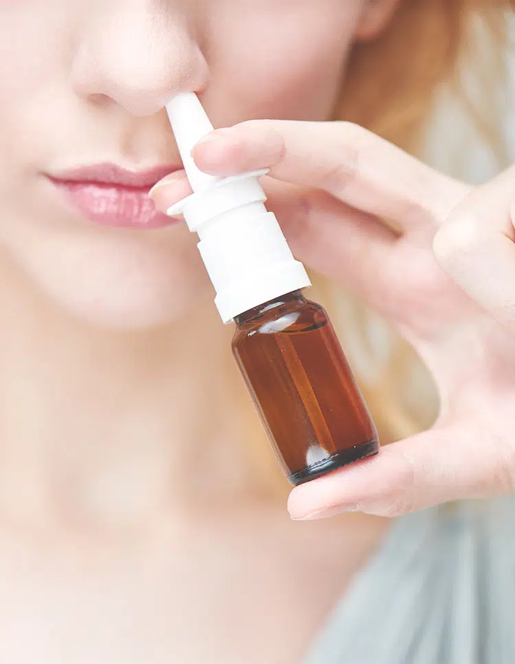 Close-up of woman using nasal spray, highlighting common nosebleed risk factors like dryness and nasal irritation.