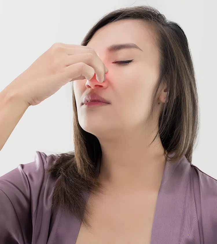 Woman pinching her nose with eyes closed, indicating a nosebleed and common symptoms like nasal bleeding and pressure.