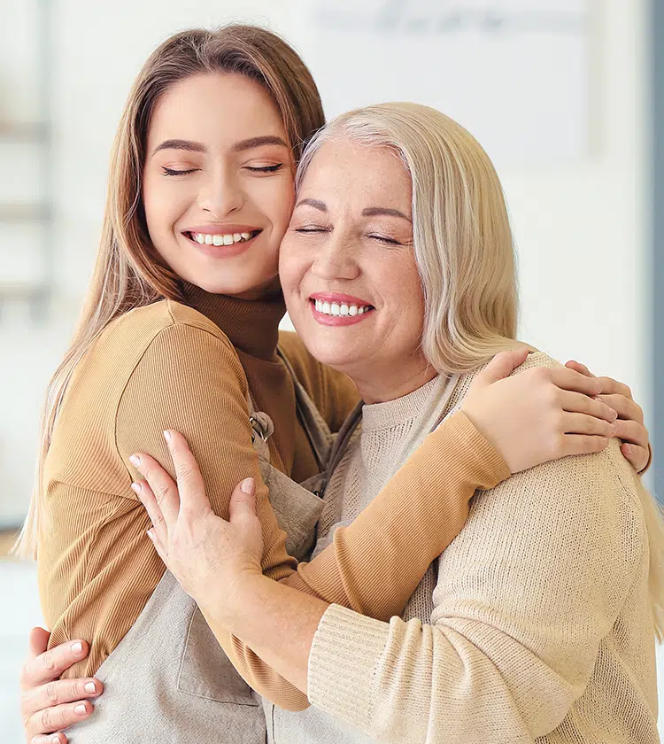 Smiling older and younger woman hugging, representing shared risk factors like allergies for post-nasal drip.
