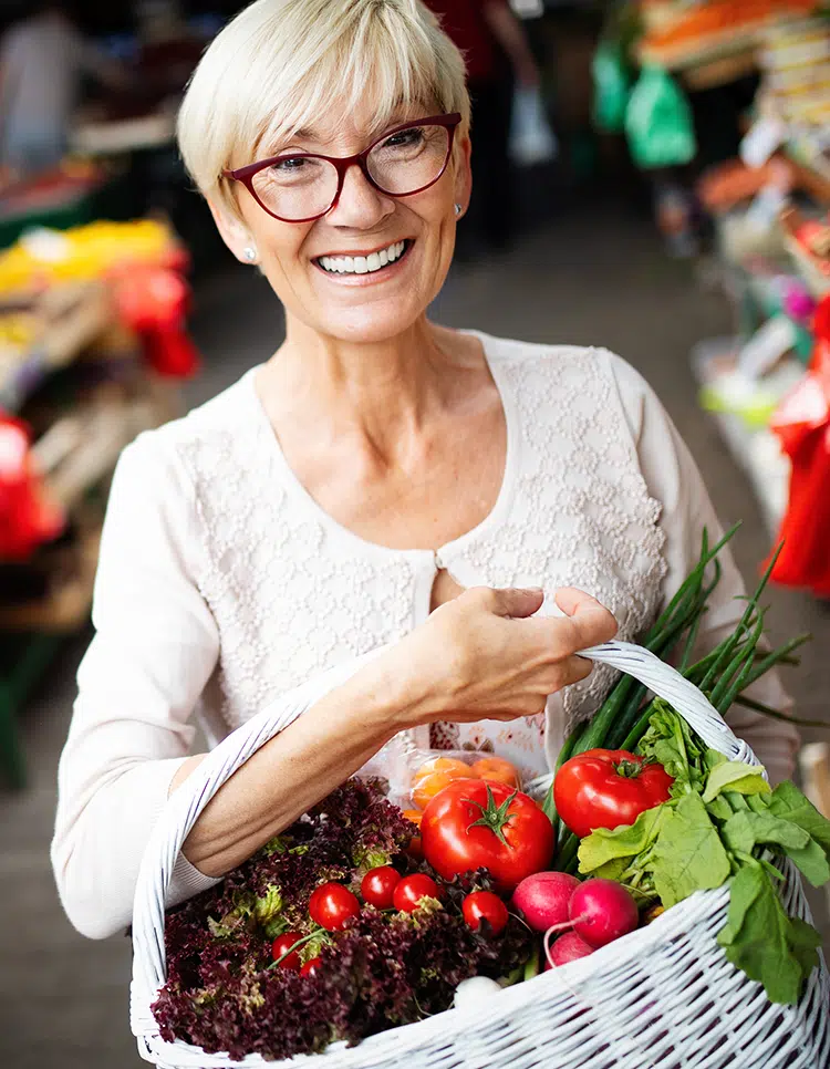 Smiling senior woman with basket of fresh vegetables, highlighting aging as a risk factor for sensory loss.