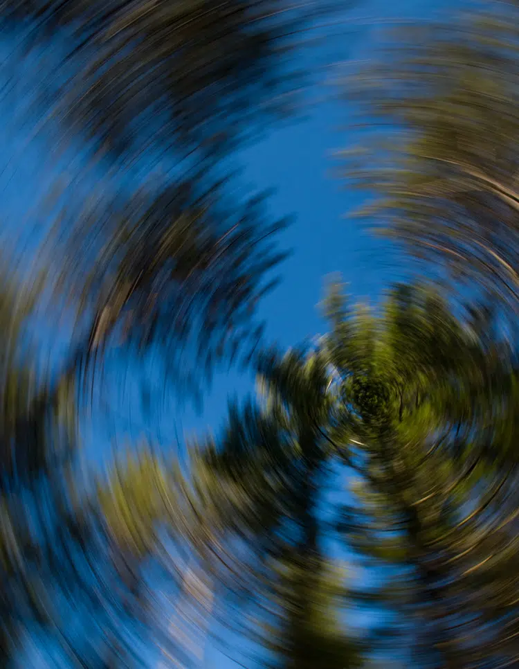 Blurred, spinning view of trees against blue sky, visually representing symptoms of dizziness and vertigo.