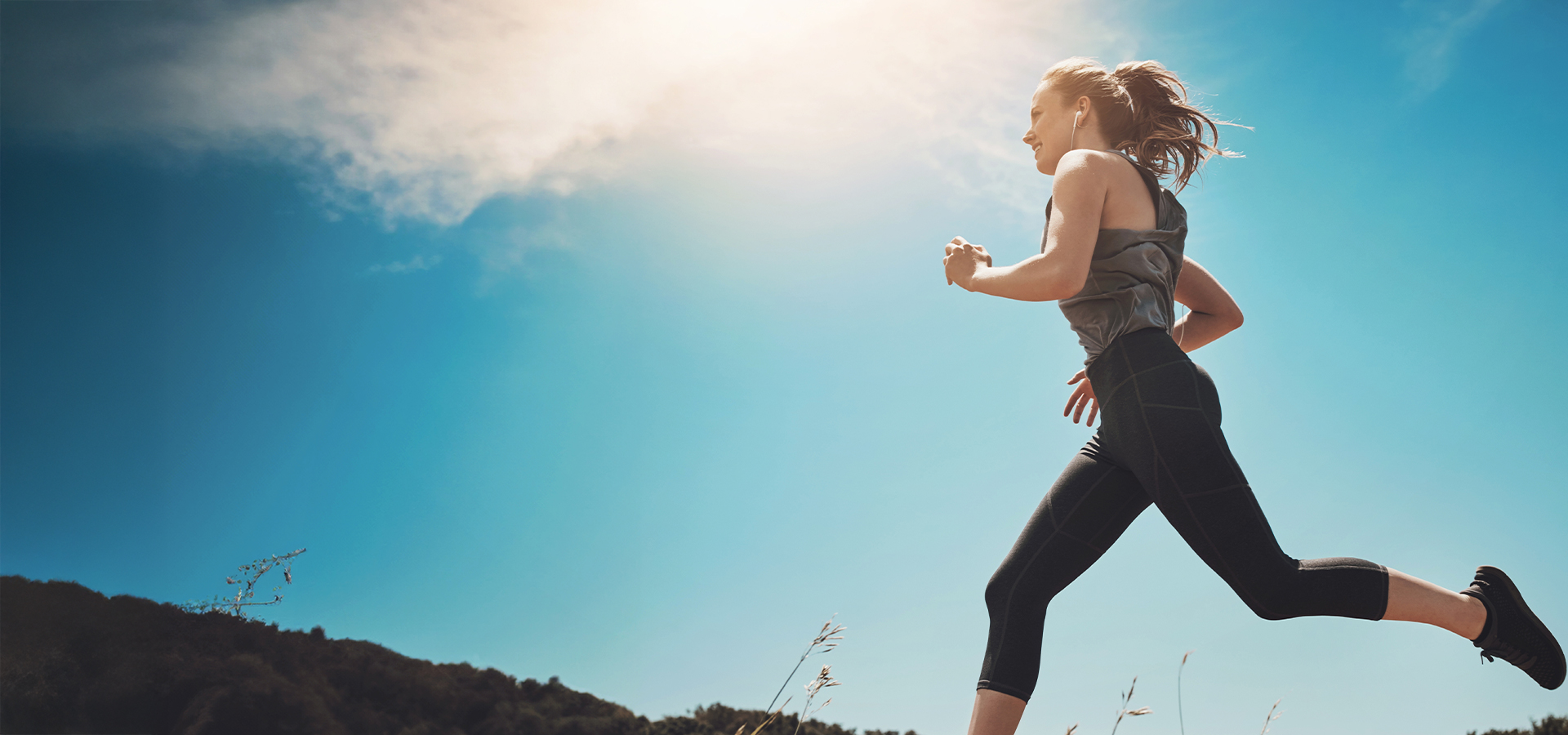 Active woman running under a clear blue sky, symbolizing recovery and improved balance after vertigo treatment.
