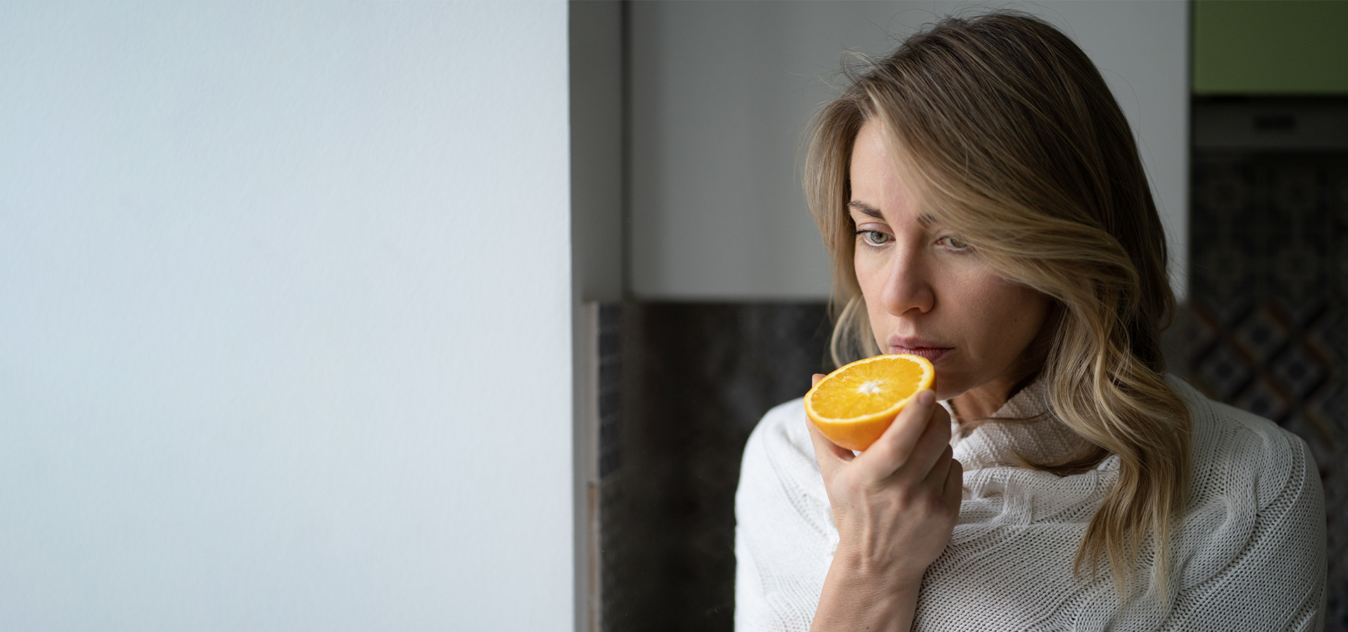 Woman holding an orange close to her nose, illustrating loss of smell and taste symptoms.