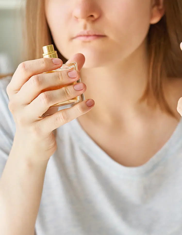 Woman attempting to smell perfume bottle, indicating early symptoms of smell and taste loss.