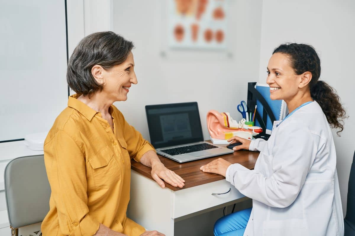 Smiling patient consulting with ENT doctor in medical office, discussing symptoms and treatment options during first visit.