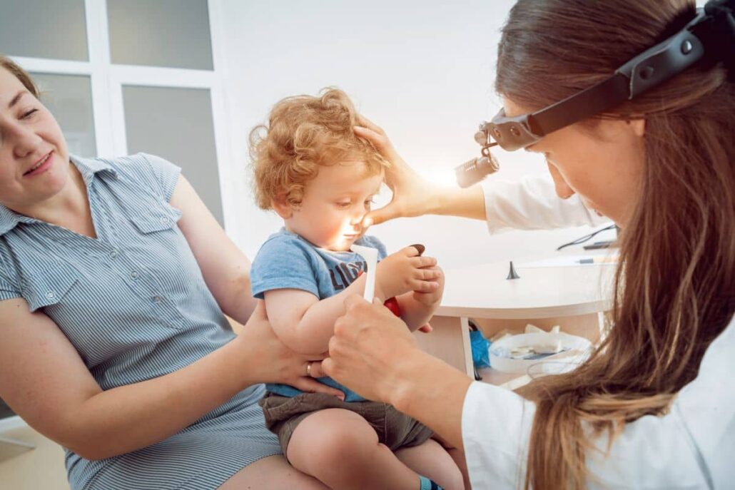 ENT specialist gently examining young child’s nose while parent holds them during calm pediatric appointment.