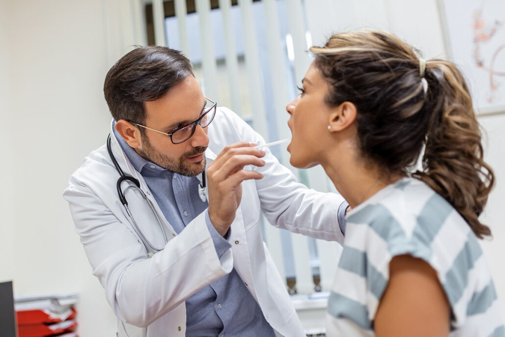 Doctor examining patient's throat for signs of peritonsillar abscess, a painful infection near the tonsils