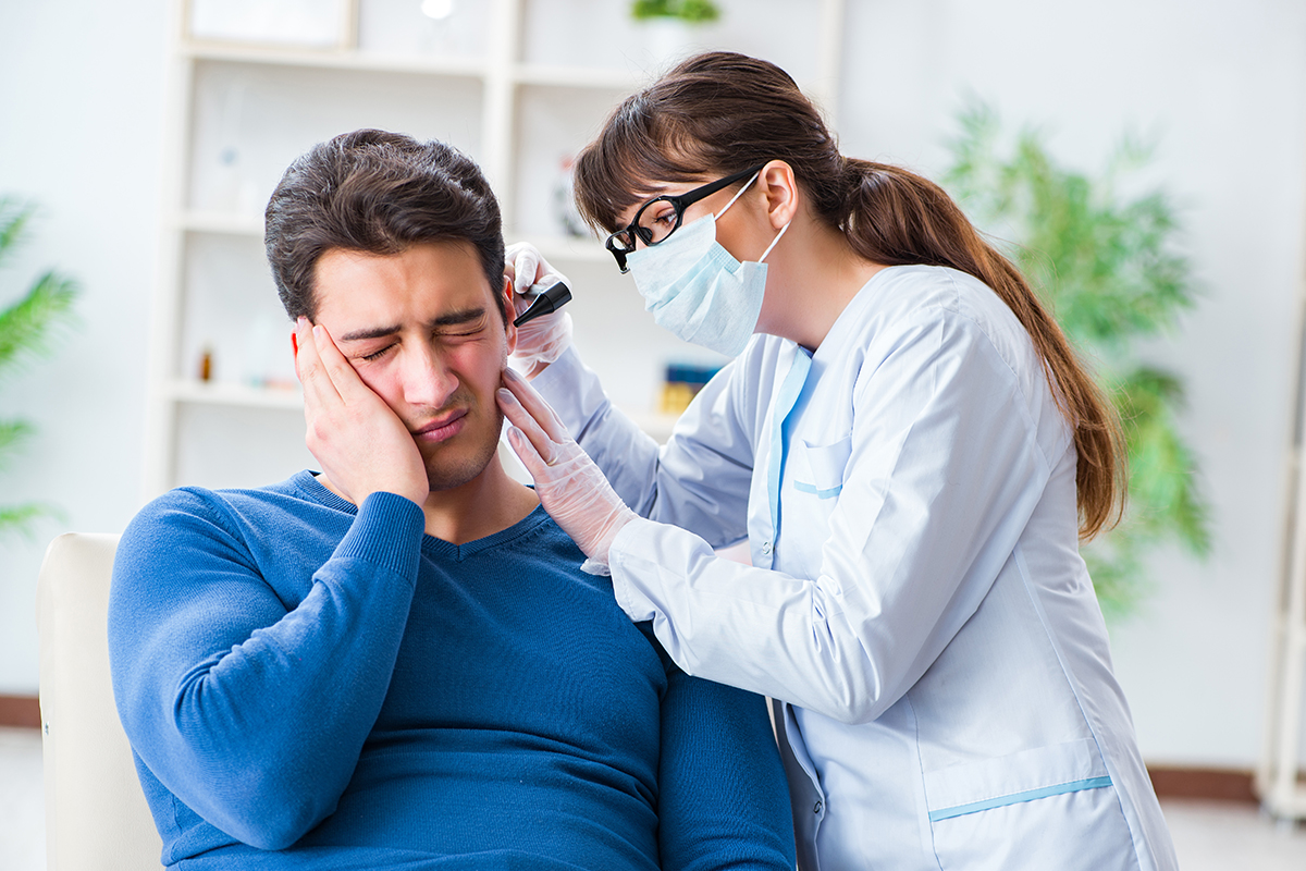 Female ENT doctor examining a male patient suffering from sudden ear pain in a clinical setting