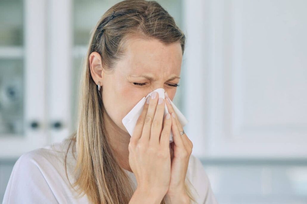 Woman holding tissue to her nose, experiencing nasal congestion and sneezing caused by mold exposure.