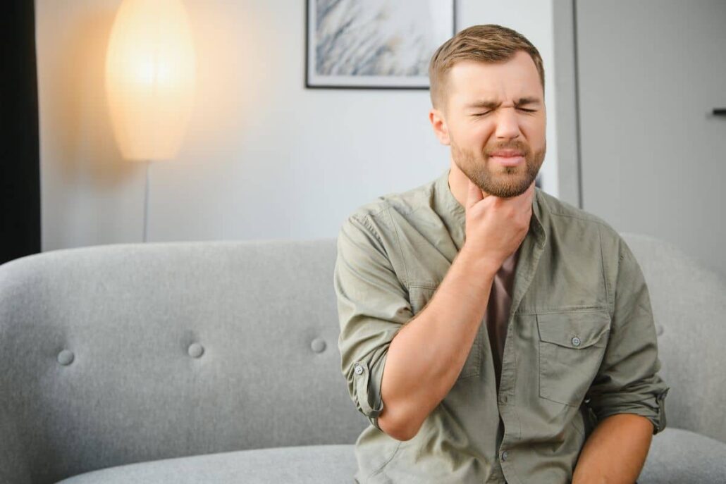 Man sitting on a couch holding his throat in discomfort, showing symptoms of mold-related irritation.
