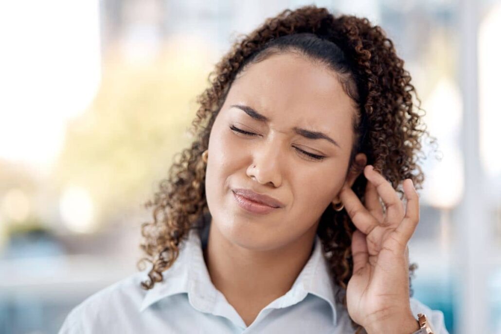 Woman touching her ear in discomfort, showing possible ear pain and pressure caused by mold exposure.