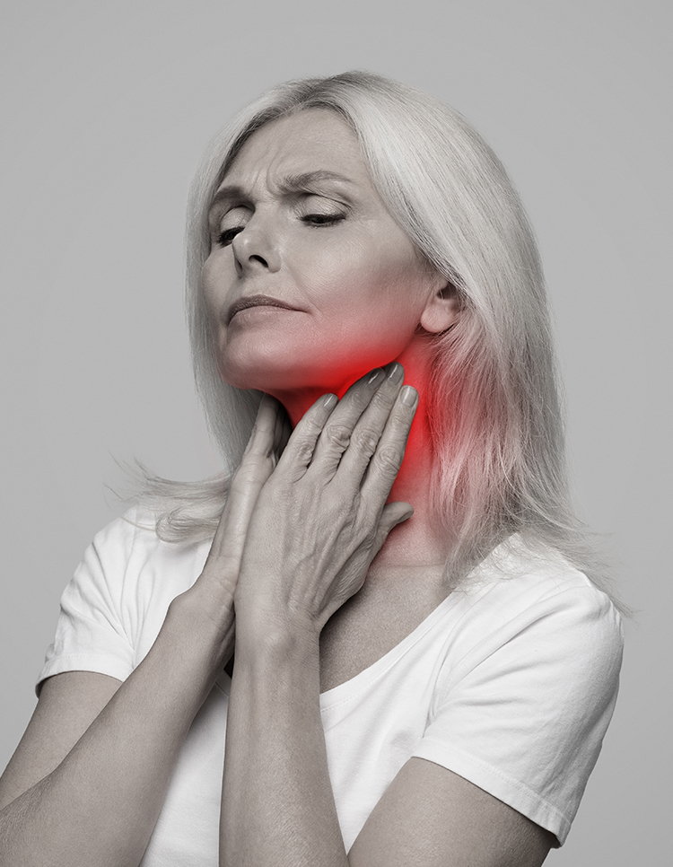 Older woman holding her throat in pain, illustrating risk factors such as infections, vocal strain, and GERD for laryngitis