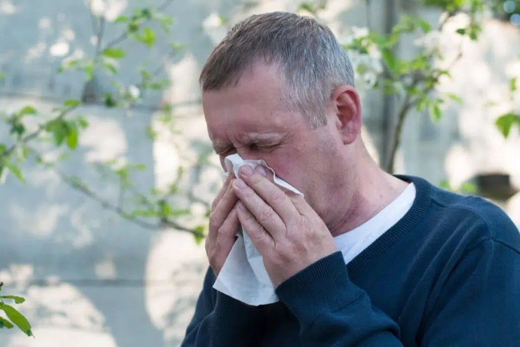 Man sneezing into tissue outdoors, showing symptoms of mold allergy such as congestion and irritation.