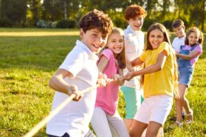 Group of smiling children playing tug of war at summer camp on a sunny day.