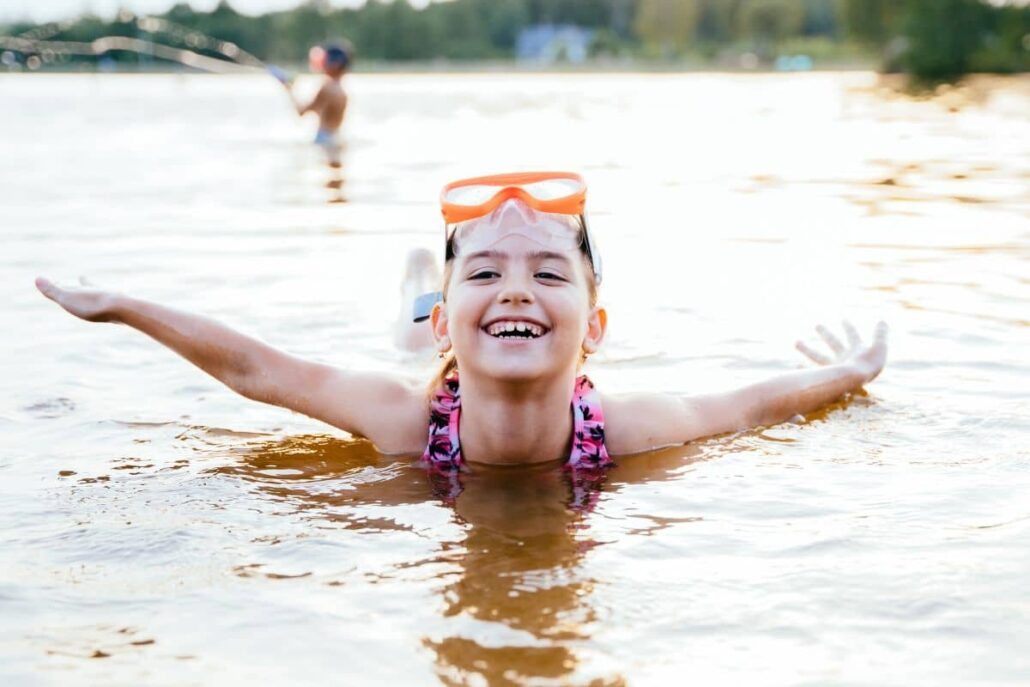 Smiling girl swimming in a lake with goggles, enjoying summer camp.
