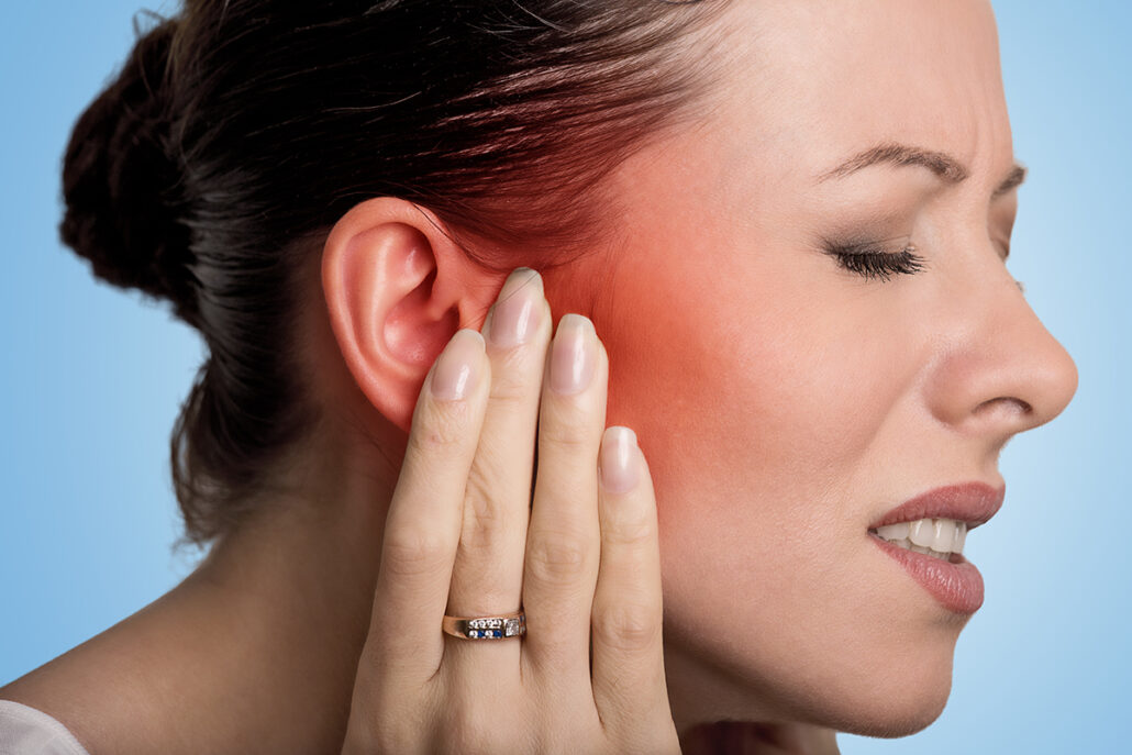 Woman holding painful ear with redness, showing symptoms of a ruptured eardrum like discomfort and hearing loss