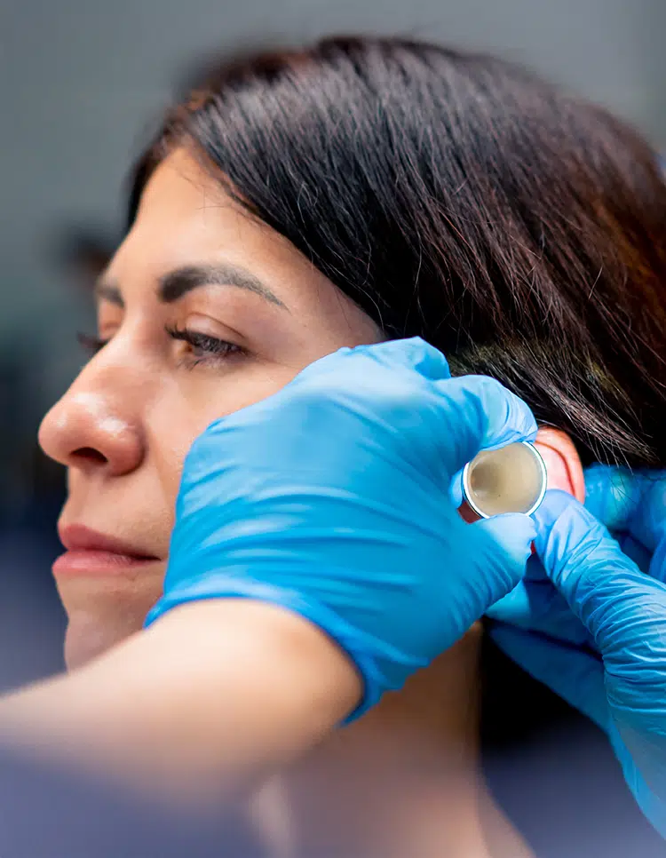 Close-up of healthcare professional examining woman’s ear with gloved hands, assessing for emergency infection symptoms