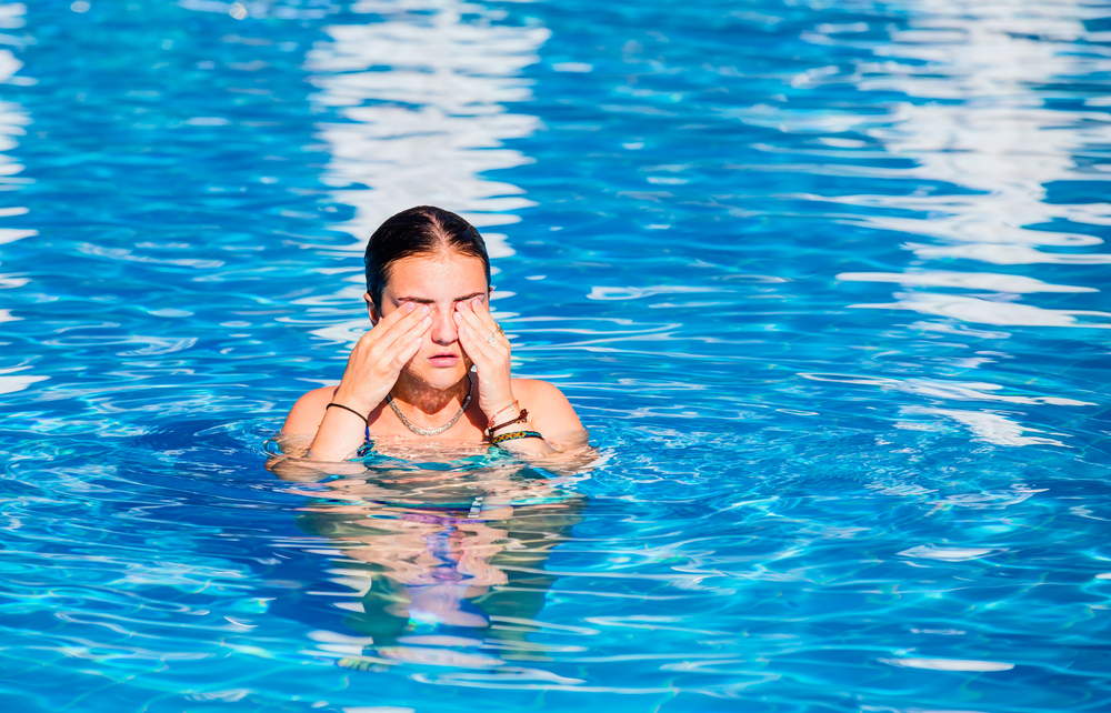 Woman in swimming pool wiping face, illustrating symptoms of aquagenic urticaria, a rare water allergy condition.