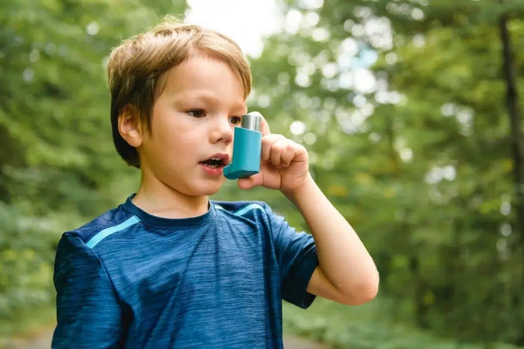 Young child using inhaler outdoors, highlighting increased asthma and sinus sensitivity to air pollution exposure