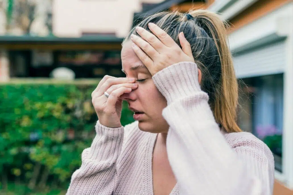 Woman pressing nose and forehead outdoors, illustrating sinus pressure and congestion linked to poor air quality