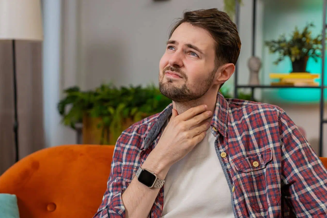 Man touching his throat indoors, illustrating seasonal ENT symptoms like sinus pressure and allergies in Marlton.