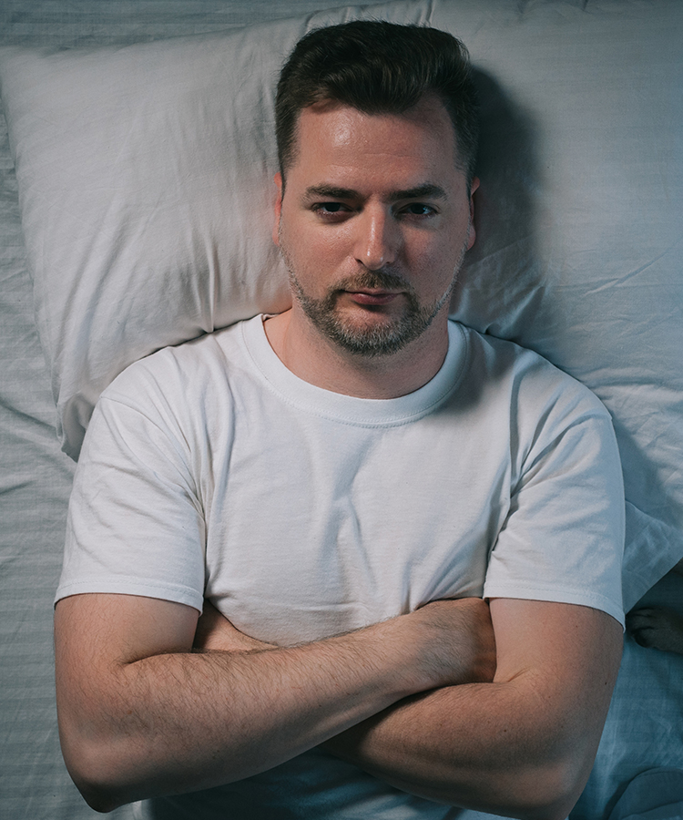 Man lying awake in bed at night, illustrating circadian rhythm misalignment and difficulty falling asleep