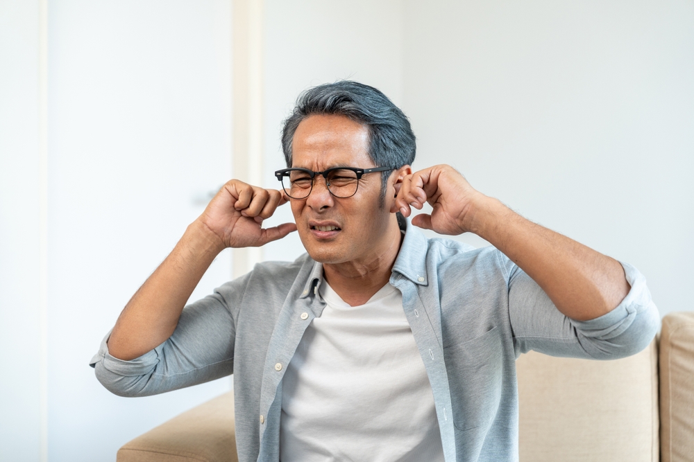 Man holding his ears with discomfort, illustrating symptoms of sudden hearing loss, ear pressure, or tinnitus.