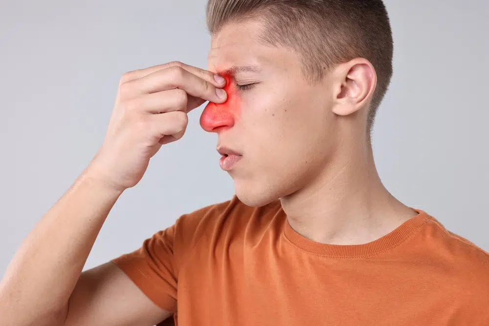 Young man pressing nose bridge with highlighted sinus pain showing facial pressure and congestion symptoms.