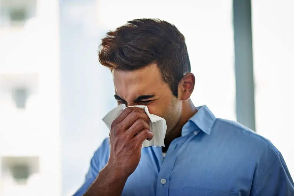 Man blowing his nose with a tissue while experiencing nasal congestion and sinus infection symptoms.