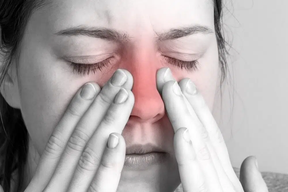 Person pressing nose and eye area showing sinus pain with redness indicating pressure and inflammation