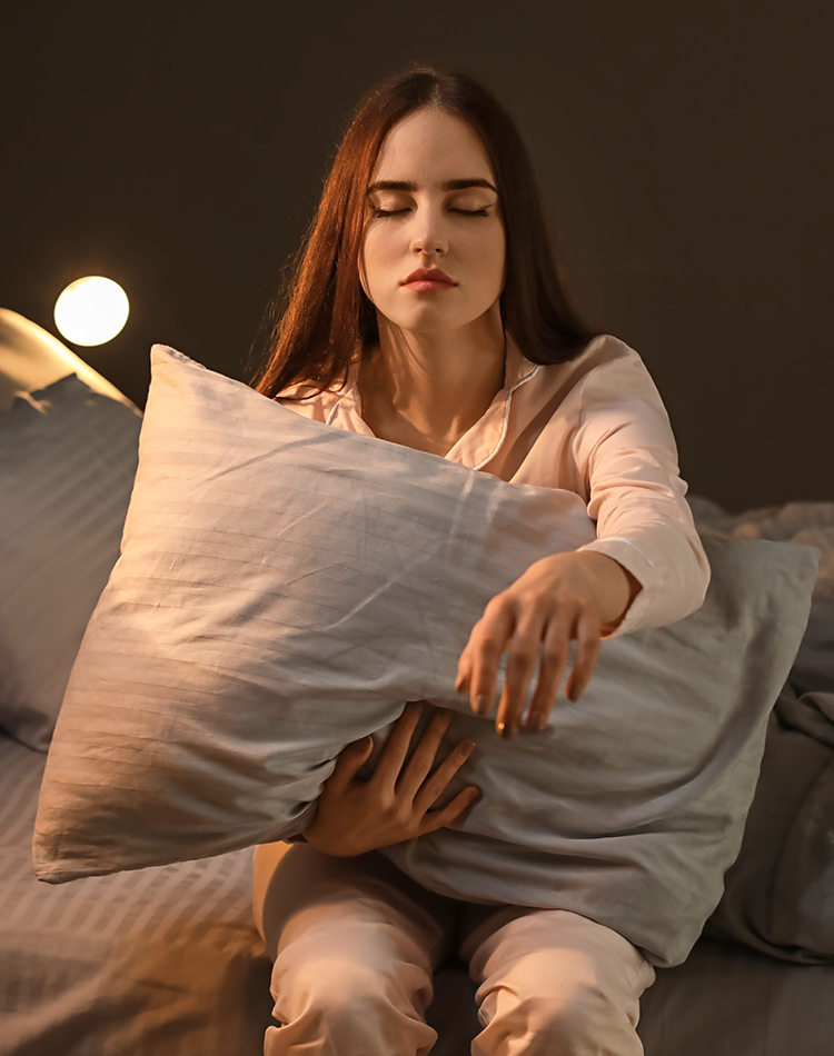Woman sitting in bed holding pillow with eyes closed, representing parasomnia evaluation during a sleep study