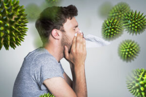 Man blowing his nose with tissue while experiencing nasal congestion, with allergy or virus particles illustrated around him.