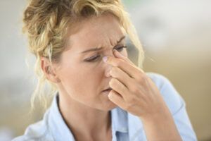 Woman pinching bridge of nose while experiencing sinus pressure and nasal pain associated with sinus infection symptoms.