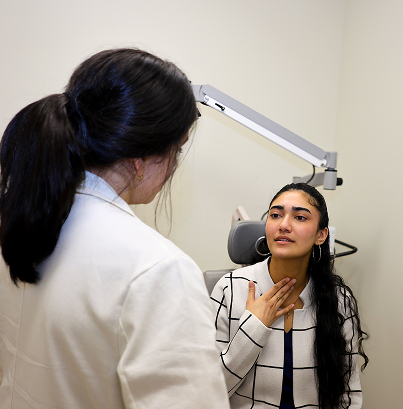 ENT specialist consulting patient pointing to throat while discussing symptoms in clinical exam room