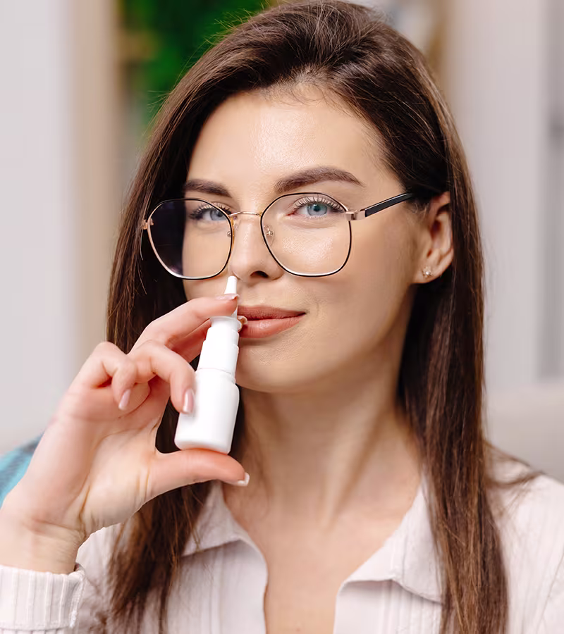 Woman using nasal spray for allergy and sinus symptoms including congestion, postnasal drip, and facial pressure.