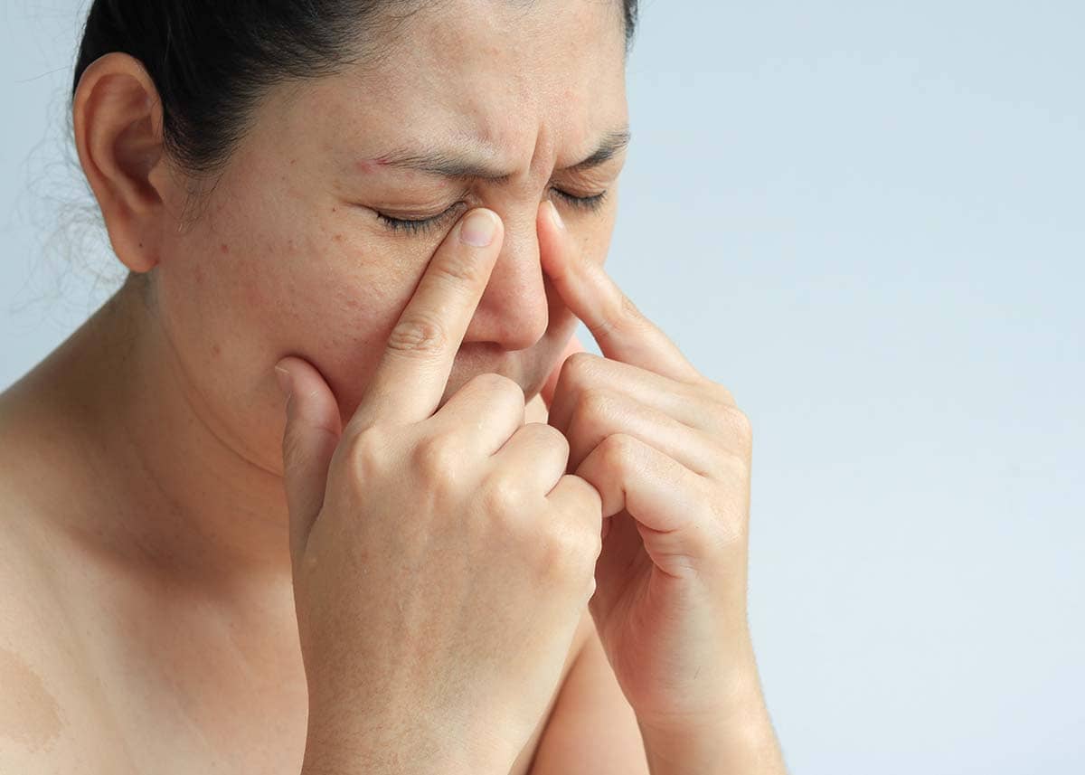 Person pressing the bridge of their nose to relieve sinus pressure and facial pain caused by sinus inflammation