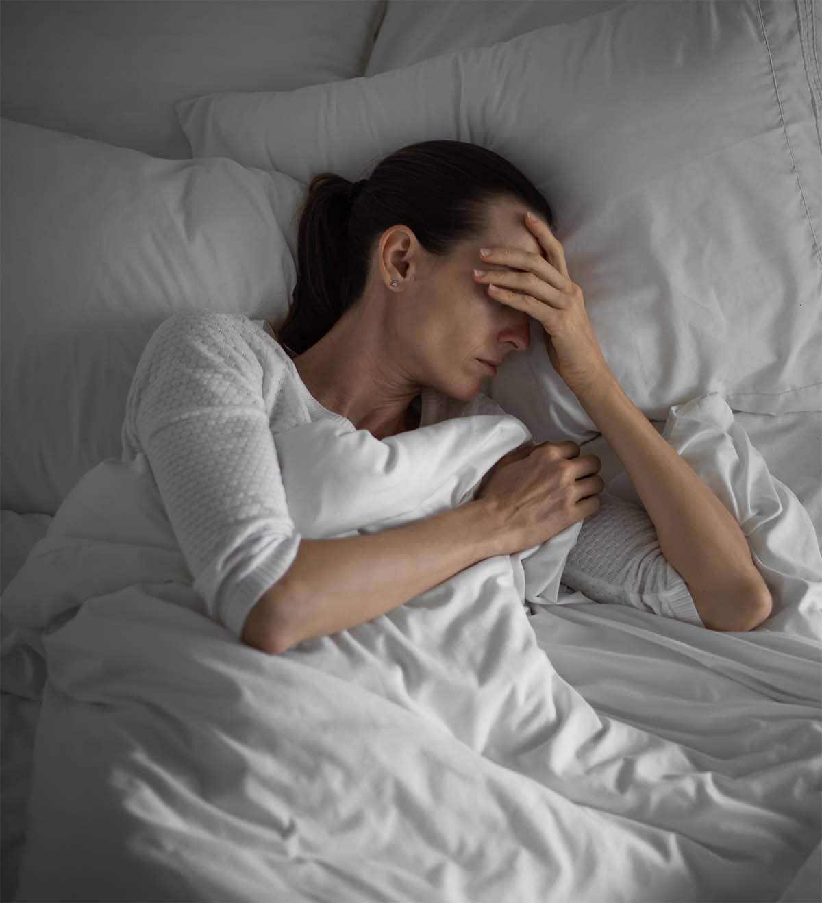 Woman lying awake in bed, illustrating behavioral, environmental, and medical factors linked to insomnia.