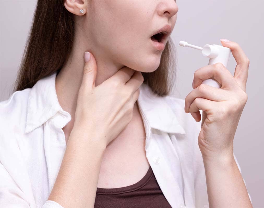 Woman using throat spray while holding her neck, illustrating treatment options for laryngitis and vocal cord care.