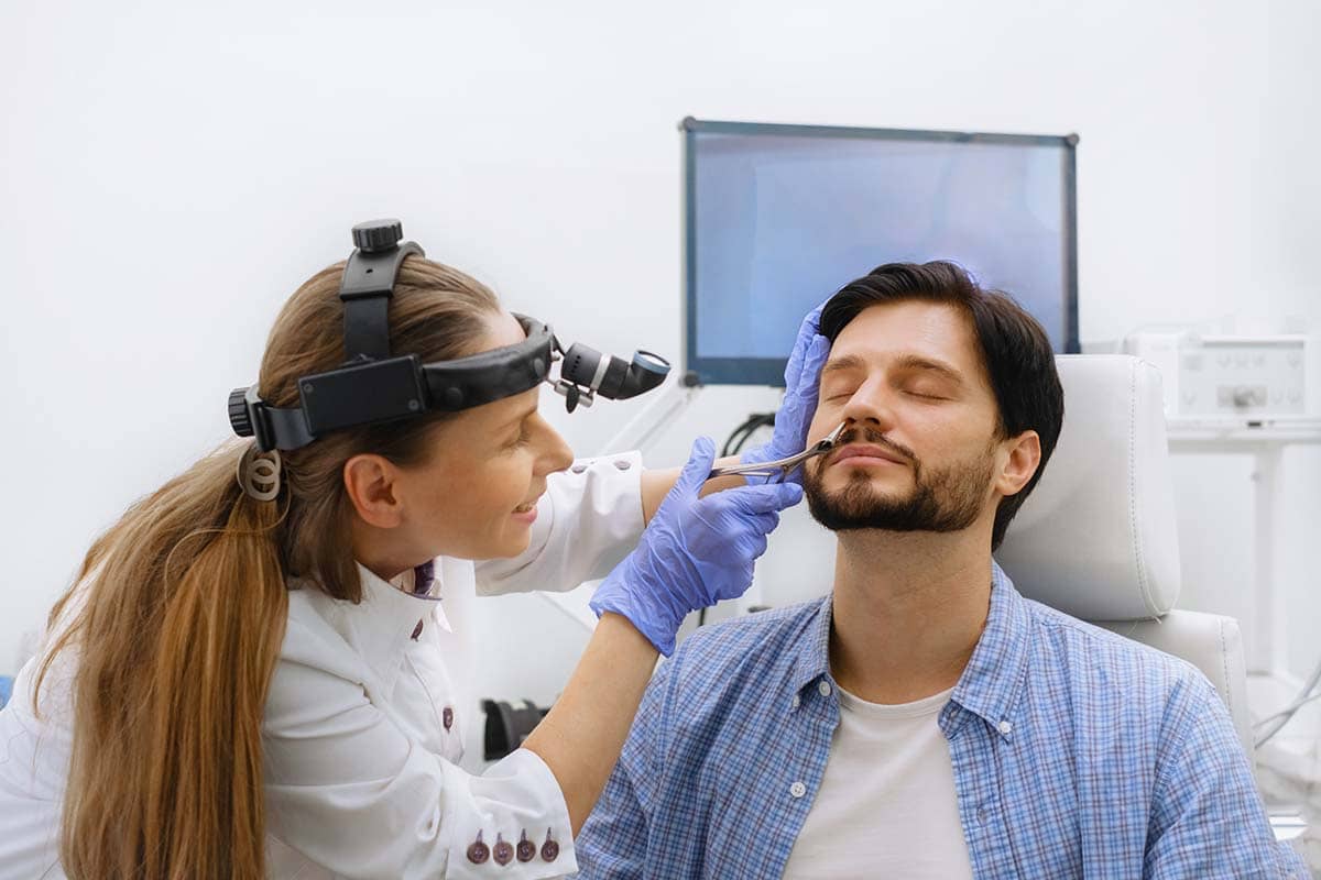 ENT specialist examining a patient’s nose during a consultation for sinus pressure and pain diagnosis.